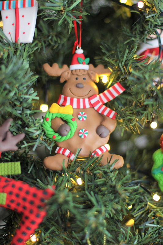 Close-up of the handmade polyclay reindeer ornament holding a wreath, hung on a festive Christmas tree.