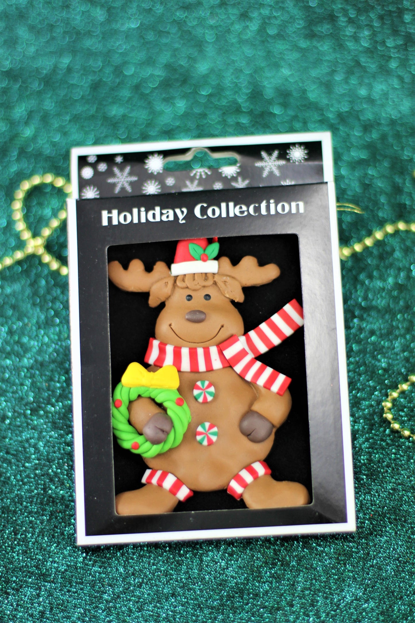 Handmade polyclay reindeer ornament holding a wreath, shown in its retail Holiday Collection box.