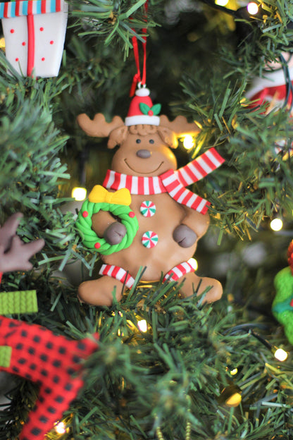 Close-up of the handmade polyclay reindeer ornament holding a wreath, hung on a festive Christmas tree.
