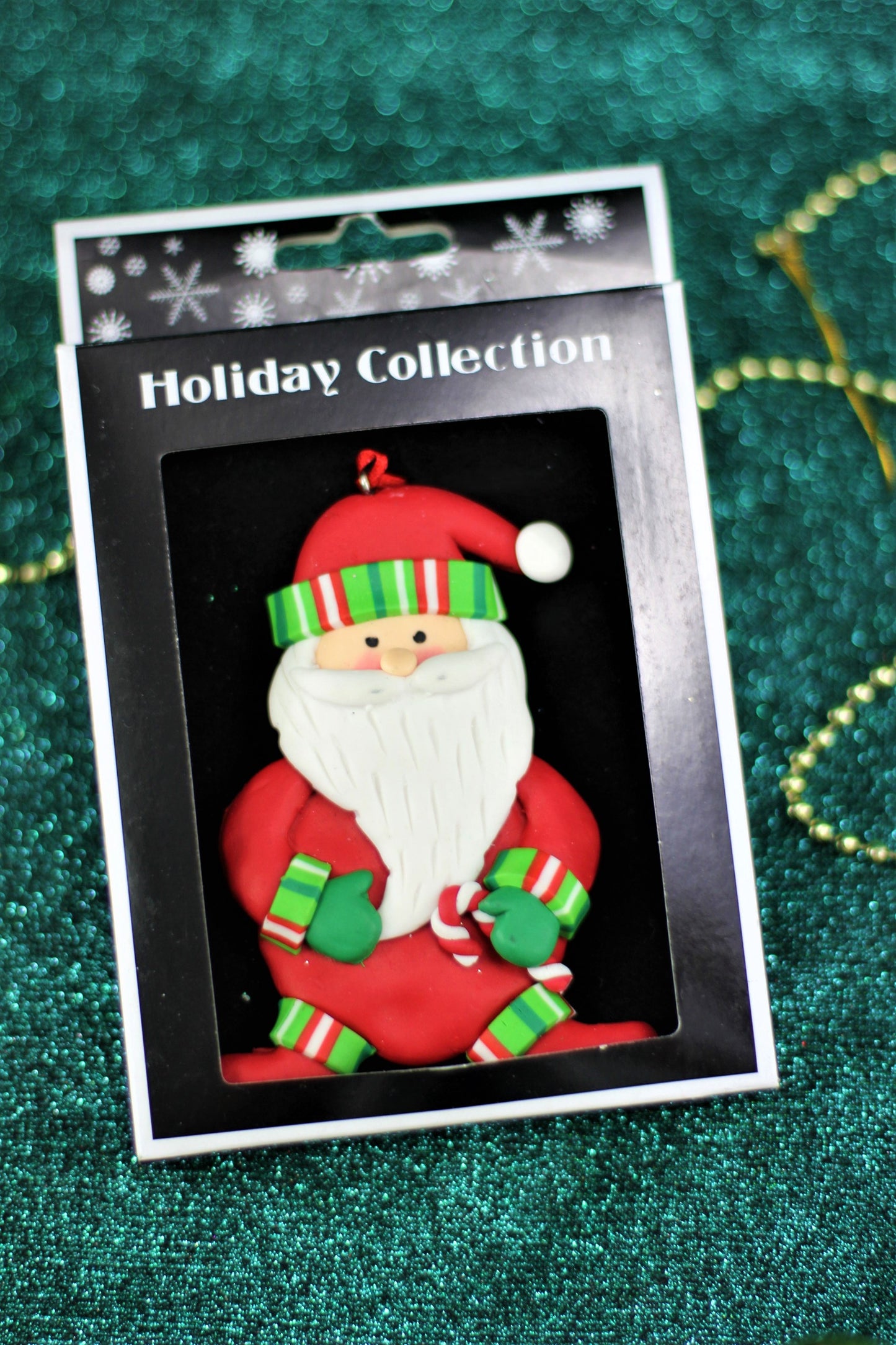 Close up of the polyclay Santa Christmas ornament in its retail Holiday Collection box packaging.
