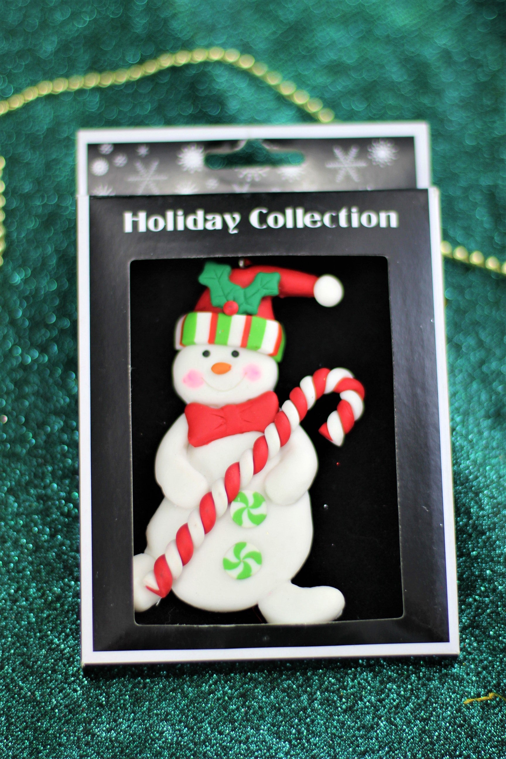 The handmade polyclay snowman ornament shown in its retail packaging box.