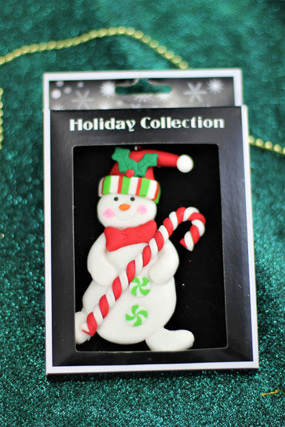The handmade polyclay snowman ornament shown in its retail packaging box.